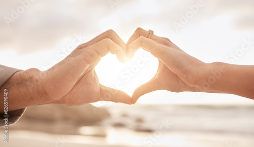 Couple, hands and heart by sunset with love on beach for honeymoon or vacation in summer with romantic gesture. Commitment, partnership and marriage with trust, promise and together in the Maldives. photo