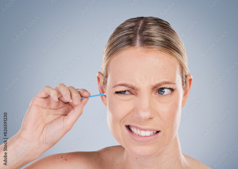 Girl, cleaning and ear for hygiene in studio for personal self care, grooming and daily routine for wellness or health. Woman, uncomfortable and isolated on grey background with cotton bud for earwax Girl, cleaning and ear for hygiene in studio for personal self care, grooming and daily routine for wellness or health. Woman, uncomfortable and isolated on grey background with cotton bud for earwax