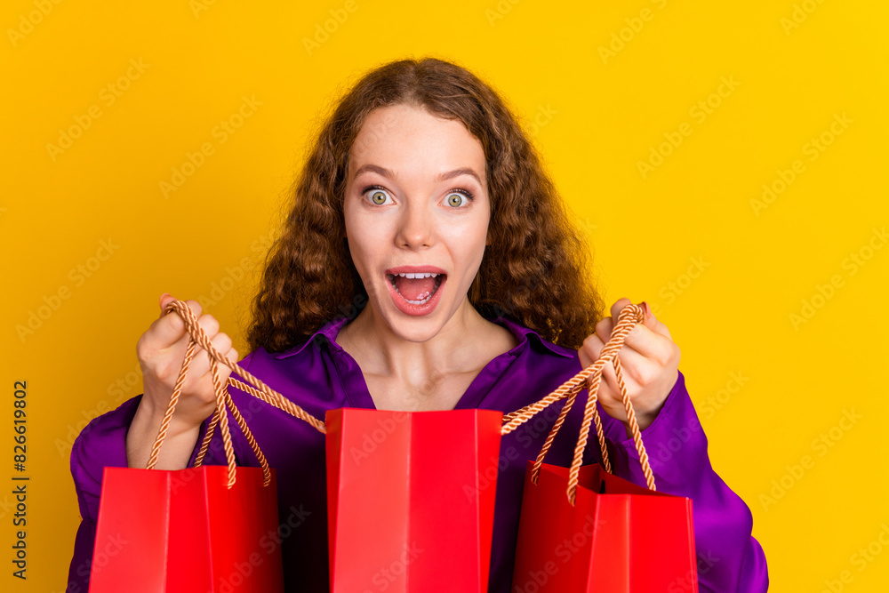 Photo portrait of lovely young lady peek interested hold shopping bags dressed stylish violet garment isolated on yellow color background