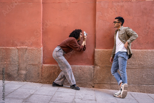 Chinese man and Hispanic woman photographing against a red wall in Madrid photo