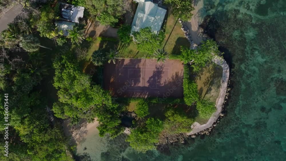 Aerial drone captures a stunning waterfront property with tennis court in Jamaica, surrounded by lush greenery and clear turquoise waters Aerial drone captures a stunning waterfront property with tennis court in Jamaica, surrounded by lush greenery and clear turquoise waters