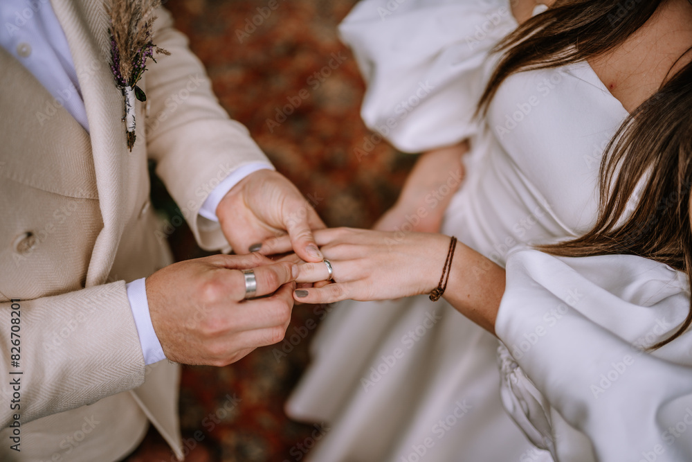 Obraz premium Riga, Latvia, - August 26, 2023 - Close-up of groom placing a wedding ring on the bride's finger during their outdoor wedding ceremony.