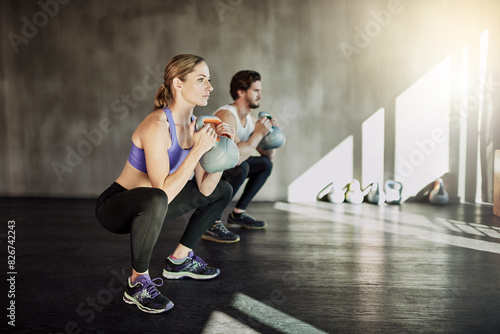 Exercise, squat and couple in gym with kettlebell, power training and workout challenge together at sports club. Man, woman or personal trainer with muscle development, healthy body and fitness.