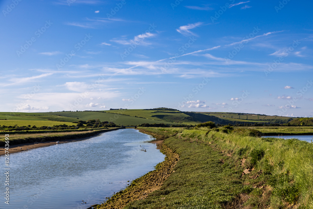 A pathway running alongside the Cuckmere River in the South Downs, with a blue sky overhead
