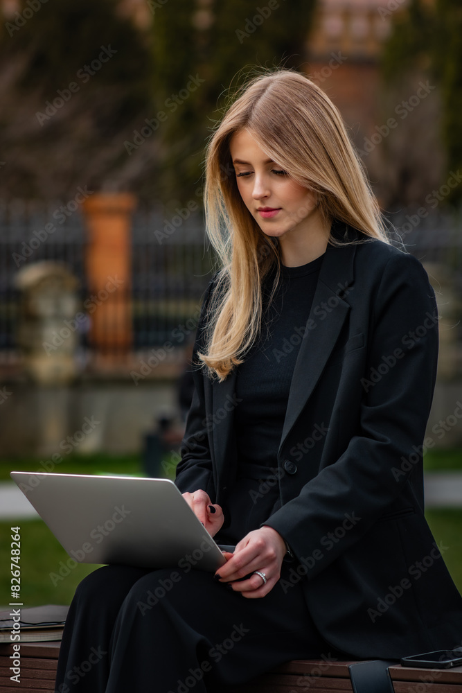 Young attractive businesswoman in black suit sitting on the bench outdoor and using laptop. Young attractive businesswoman in black suit sitting on the bench outdoor and using laptop.
