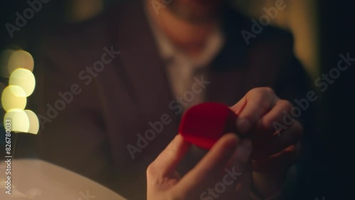Enamoured guy proposing engagement opening gold ring box at night hotel closeup photo