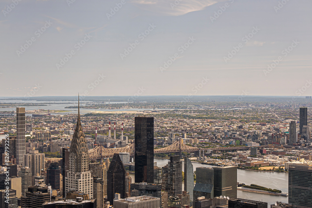 Obraz premium New York, NY, USA - August 2, 2023: Ed Koch Queensboro Bridge over East River partly hidden by Chrysler Building and other skyscrapers as seen from Empire State Building. Wide landscape behind under b