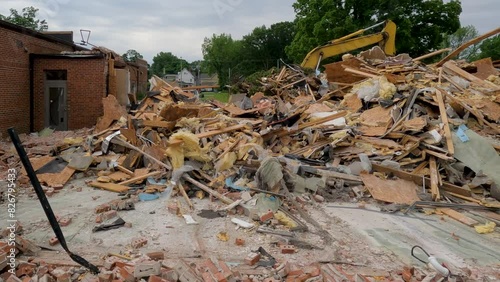 Panning views of a completely demolished building at a demolition construction site. Piles of rubble are all that remain of the brick building. Heavy construction equipment in the background of view. 