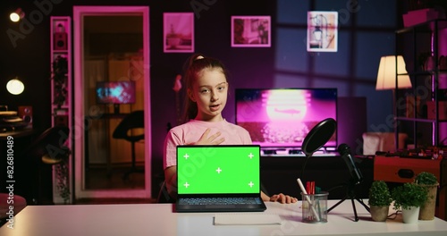 Young girl tech content creator filming technology review of green screen laptop, unboxing it and presenting specifications to audience. Cute gen Z influencer showing mockup notebook device to viewers