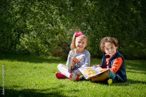 Irmão sentados no gramado brincando e lendo livro, leitura infantil