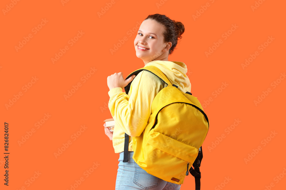 Beautiful young woman in stylish hoodie with backpack and books on orange background Beautiful young woman in stylish hoodie with backpack and books on orange background