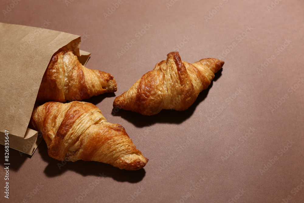 Paper bag with tasty croissants on brown background Paper bag with tasty croissants on brown background