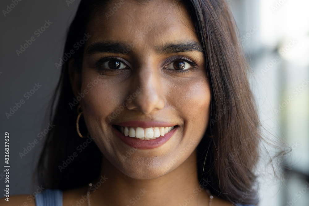 In a modern office, a young Indian woman with long dark hair and brown eyes warmly smiles In a modern office, a young Indian woman with long dark hair and brown eyes warmly smiles