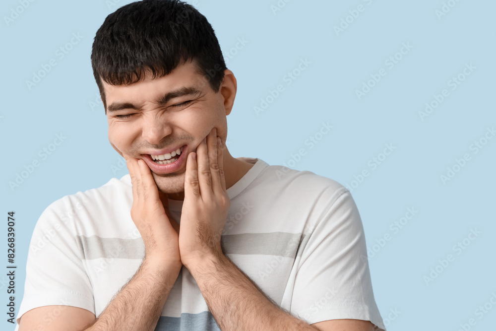 Young man suffering from toothache on blue background, closeup Young man suffering from toothache on blue background, closeup