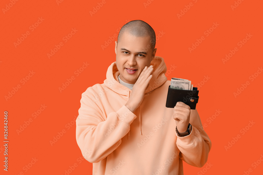 Young man with full wallet telling secret on orange background Young man with full wallet telling secret on orange background
