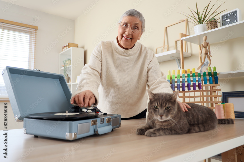 Senior woman with cute cat and record player listening to music at home Senior woman with cute cat and record player listening to music at home