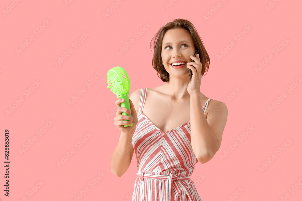 Young woman with mini green electric fan using mobile phone on pink background Young woman with mini green electric fan using mobile phone on pink background
