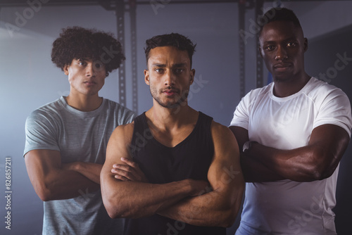 At gym, three young fit diverse men standing confidently with arms crossed photo