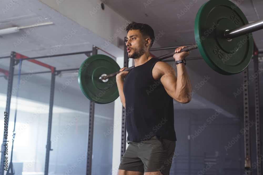 At gym, biracial man lifting weights, looking strong and fit in modern gym At gym, biracial man lifting weights, looking strong and fit in modern gym