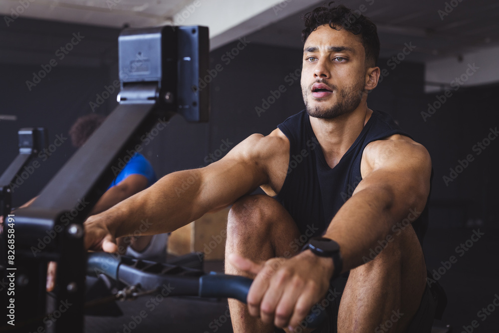 At gym, strong and fit biracial man using rowing machine, focused on workout At gym, strong and fit biracial man using rowing machine, focused on workout