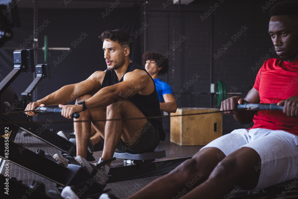 At gym, three young diverse men working out on rowing machines At gym, three young diverse men working out on rowing machines
