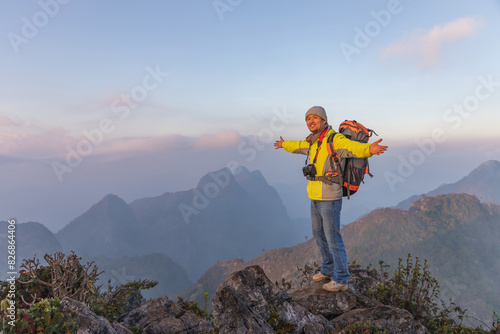 Cheerful smiling male photographer with dslr camera on top hills raised hands