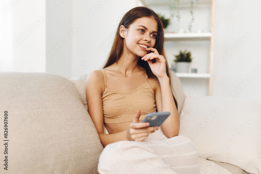 Happy Woman Holding Mobile Phone and Smiling While Relaxing on Cozy Sofa at Home Happy Woman Holding Mobile Phone and Smiling While Relaxing on Cozy Sofa at Home