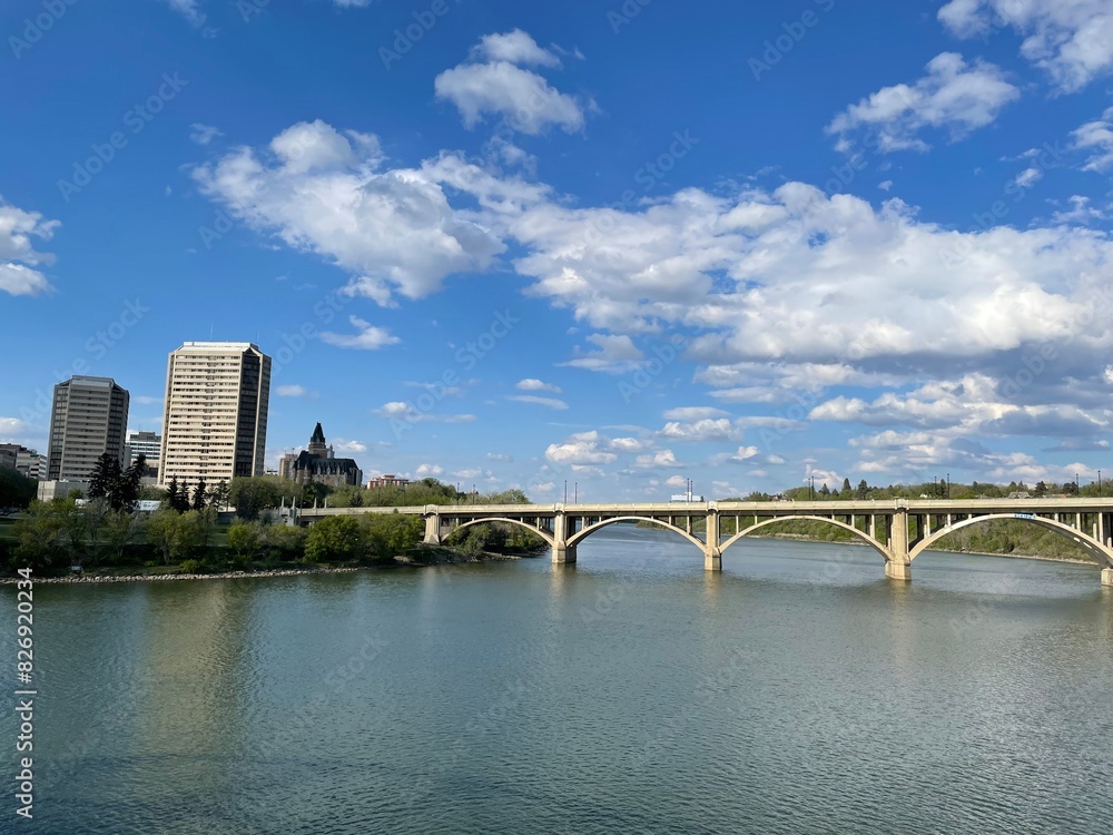 Naklejka premium Puente sobre río y ciudad de fondo con cielo azul y algunas nubes. 