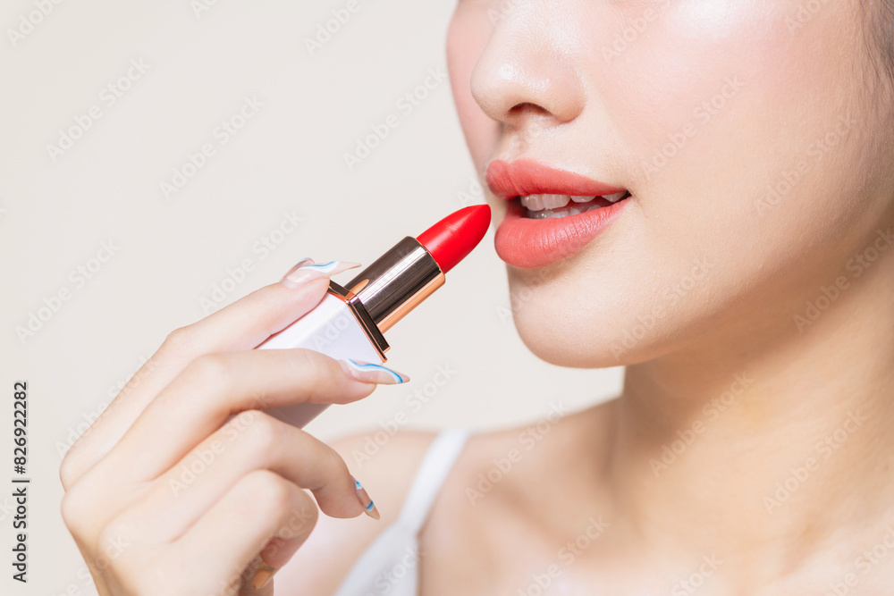 pretty asian woman using a red lipstick on beige background
