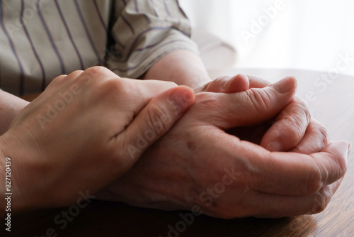 机の上で高齢女性の手を握る女性の手元