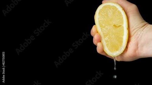 Hand squeezing lemon juice from half a lemon on a black background slow motion.