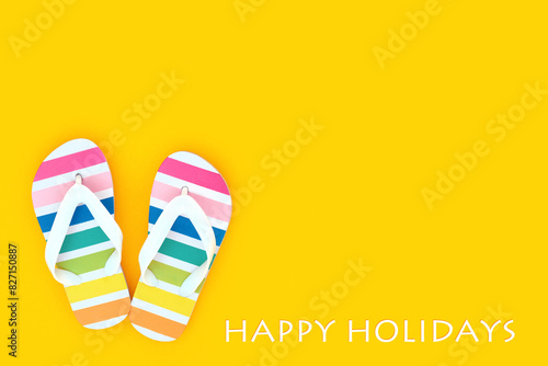 Rainbow flip flops for happy holidays concept. Casual summer footwear on yellow background. Beach seaside vacation with trans and LGBT themed concept with text.