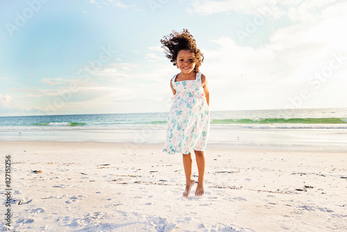 Young girl with curly hair jumping on the beach, smiling brightl photo