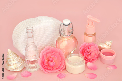 Rose flower skincare products for sensitive skin on pink. Natural pure feminine health spa treatment with moisturizer, aromatherapy oil, rosewater, shells and flowers.