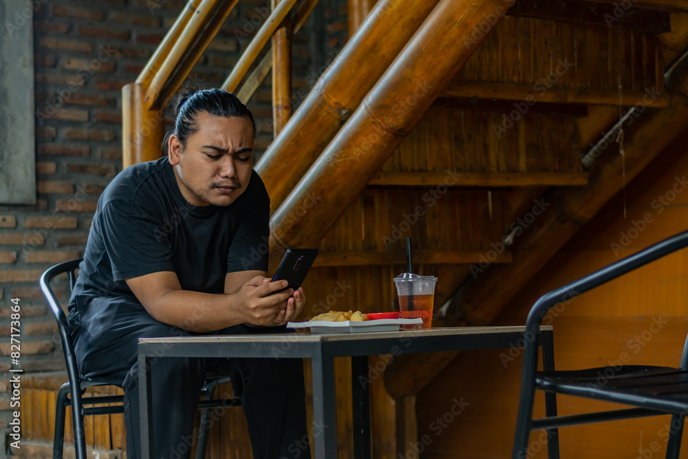 Young Asian man, digital nomad working remotely from cafe, using laptop and smartphone. young Asian men are hanging out in a cafe with an industrial theme