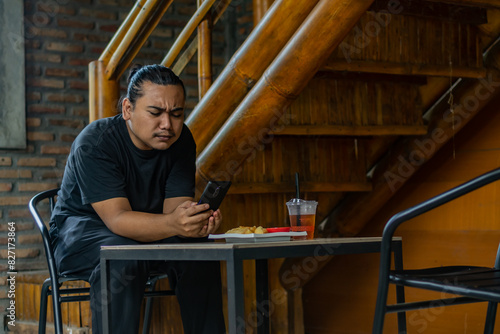 Young Asian man, digital nomad working remotely from cafe, using laptop and smartphone. young Asian men are hanging out in a cafe with an industrial theme