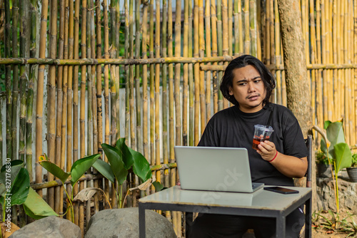 Young asian men, digital nomad working remotely from a cafe, drinking coffee and using laptop.