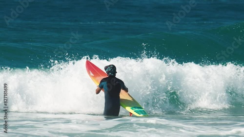 Surfer walks into the ocean with surfing board