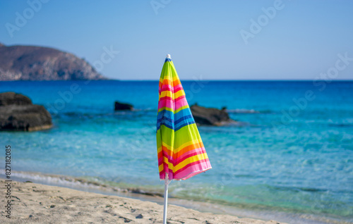 closed umbrella of a thousand colors on the beach in front of the sea and the blue sky