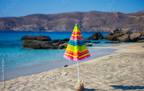a beach umbrella with a thousand colors like a rainbow in front of the blue sea