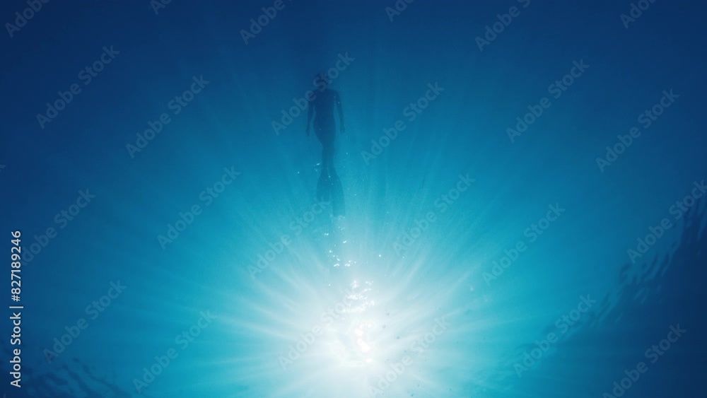 Woman swims on the surface of the tropical sea. Bottom underwater view of the young woman swimming in the sea at sunny day Woman swims on the surface of the tropical sea. Bottom underwater view of the young woman swimming in the sea at sunny day