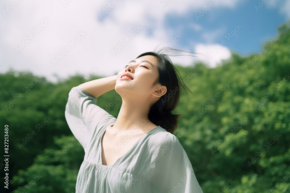 Low angle portrait of relaxed young Asian woman with her eyes closed stretching arms in the nature, setting herself free and feeling relieved Low angle portrait of relaxed young Asian woman with her eyes closed stretching arms in the nature, setting herself free and feeling relieved