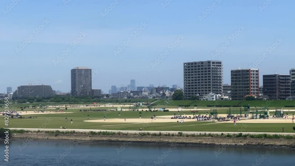 People enjoy a sunny day at a riverside park with city skyline in the background