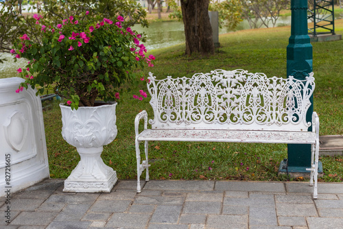 White openwork bench and flowerpot with blooming pink bougainvillea in a summer park