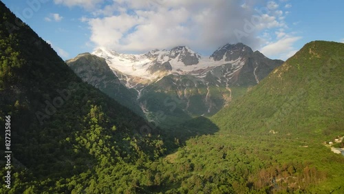 Digor Gorge in North Ossetia, Caucasus, Russia. Snow-covered mountain peaks and green forest at sunny morning. Aerial view. Summer landscape.  
 photo