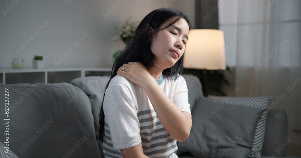 Portrait of Unwell young woman has neck pain while sitting on the sofa in the living room. People with muscle-body problems Portrait of Unwell young woman has neck pain while sitting on the sofa in the living room. People with muscle-body problems