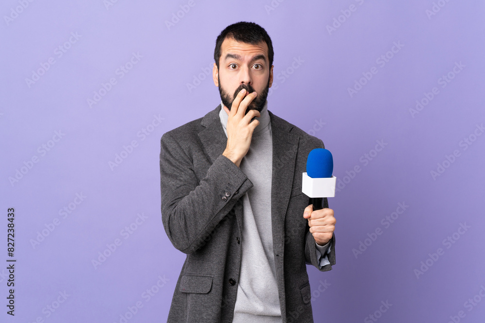 Naklejka premium Adult reporter man with beard holding a microphone over isolated purple background surprised and shocked while looking right