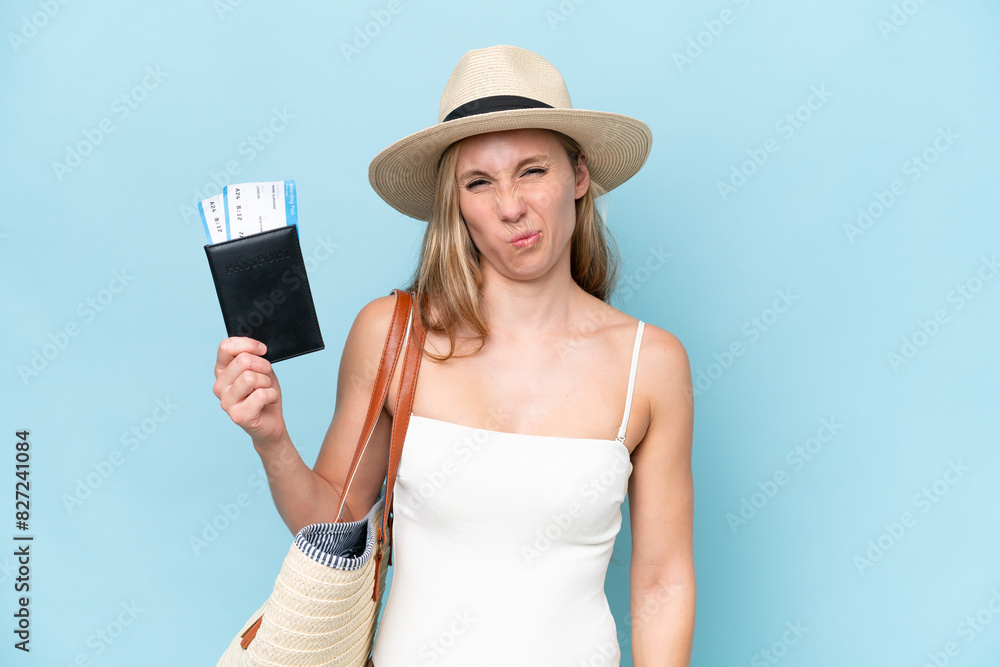 Young blonde woman in swimsuit holding passport isolated on blue background with sad expression Young blonde woman in swimsuit holding passport isolated on blue background with sad expression