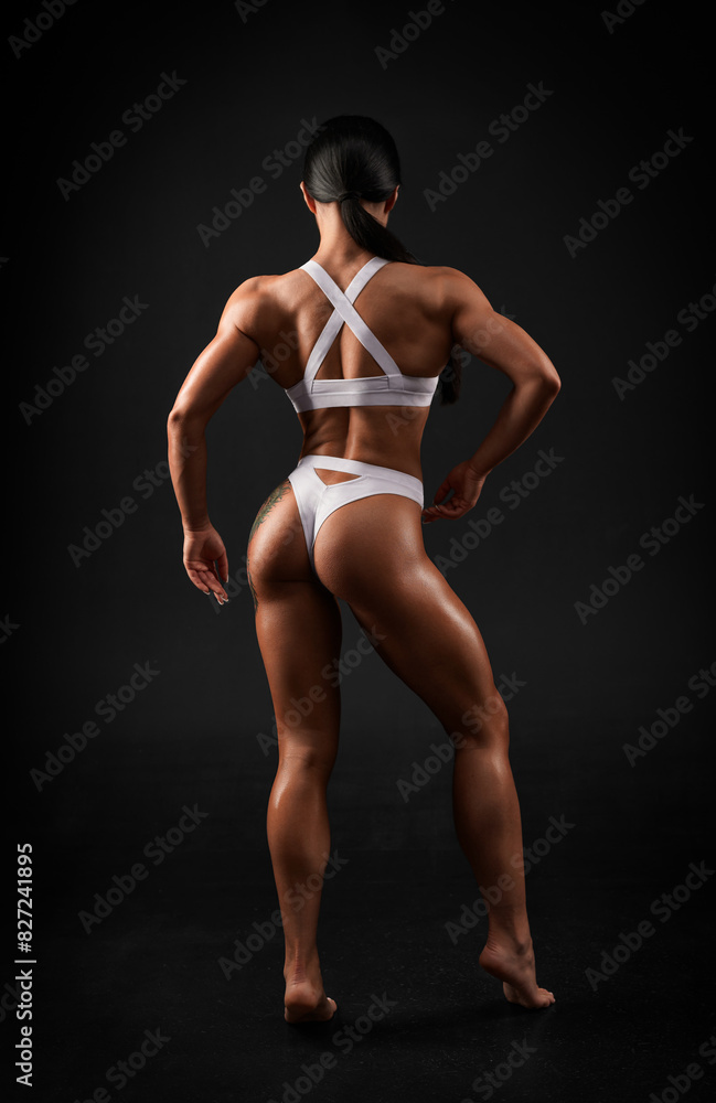 Image of a sexy sports woman in a black studio. Sports underwear. Trained body. Back view.