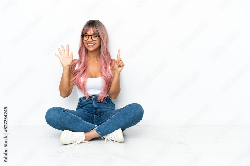 Young mixed race woman with pink hair sitting on the floor isolated on white background counting six with fingers Young mixed race woman with pink hair sitting on the floor isolated on white background counting six with fingers